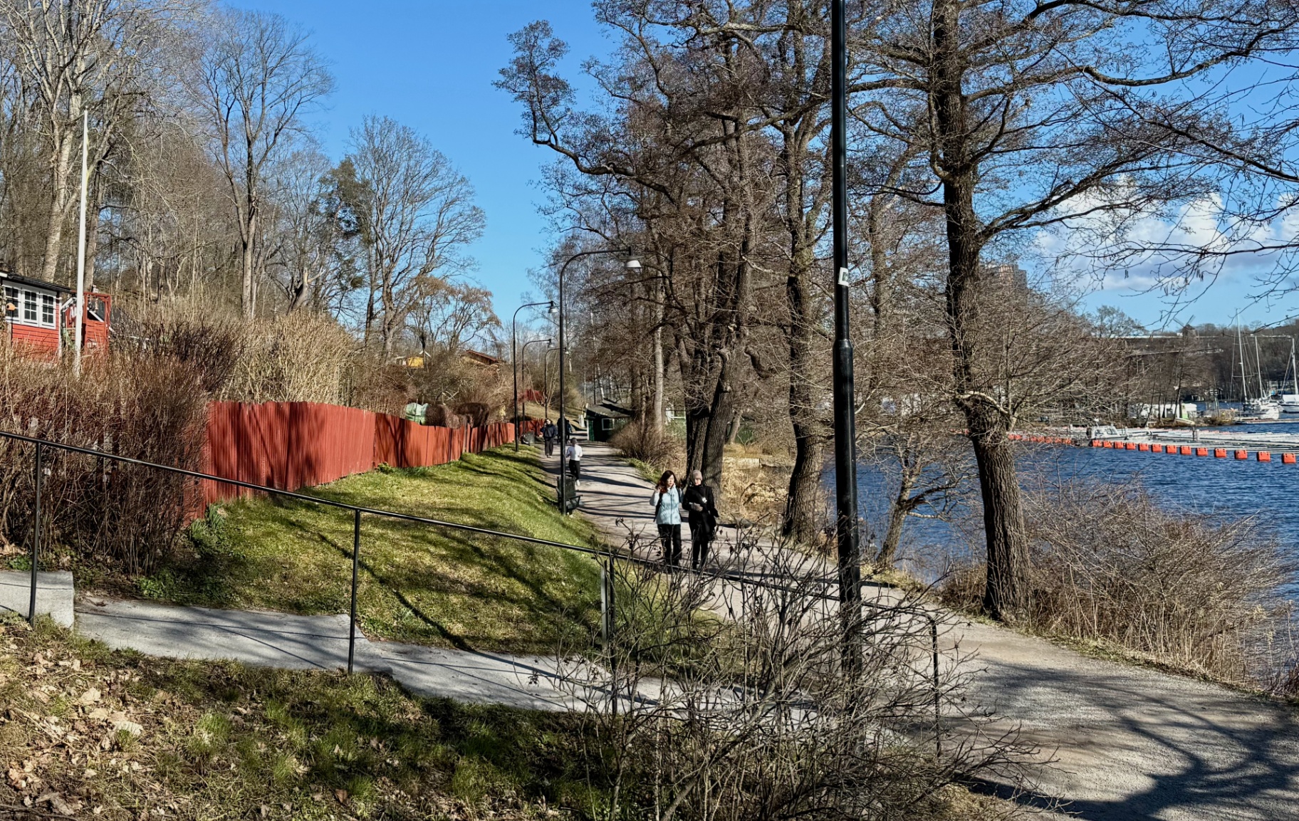 Två personer promenerar längs Årstaviken i vårsol